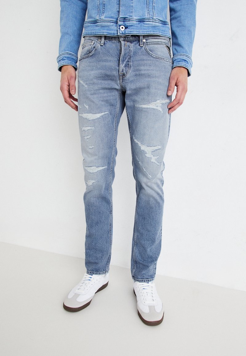 Ljusblå, slitna jeans med flera hål, smal passform och en urtvättad textur, kombinerat med vita sneakers.