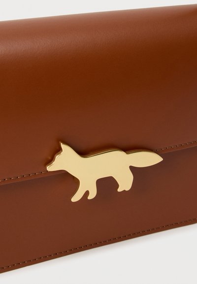 Καφέ δερμάτινο πορτοφόλι με μεταλλική πόρπη σε σχήμα αλεπούς χρυσού χρώματος μπροστά, που δείχνει λεπτομερείς ραφές στις άκρες.
