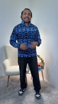 Fleece pullover in blue with a geometric pattern, featuring a high collar and a half-zip. Black jeans and black-and-white sneakers complete the outfit.