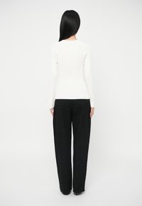 Λευκή ριμπ μπλούζα με μακριά μανίκια συνδυασμένη με χαλαρούς μαύρους παντελόνες που έχουν υφασματική υφή και λεπτές γυαλιστερές λεπτομέρειες.