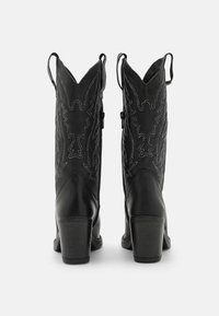 Bottes de cowboy en cuir noir avec un talon haut, présentant des motifs de couture complexes, une pointe allongée et des tirants en haut pour un enfilage facile.