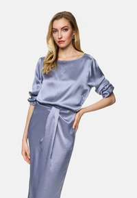 Satin blouse and skirt set in light blue. Blouse features a boat neck and rolled sleeves; skirt has a tied waist detail, smooth texture.