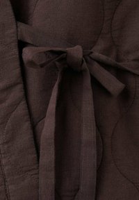 Brauner Leinenstoff mit gestepptem Muster, einem gebundenen Gürtel und einem dezenten kreisförmigen Design. Das Gesamtdesign ist weich und fällt elegant.