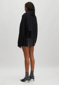 Zwarte oversized trui met een hoge hals, gestyled met een glanzende zwarte mini-jurk. Aangevuld met grijze sokken en puntige zwarte hakken.