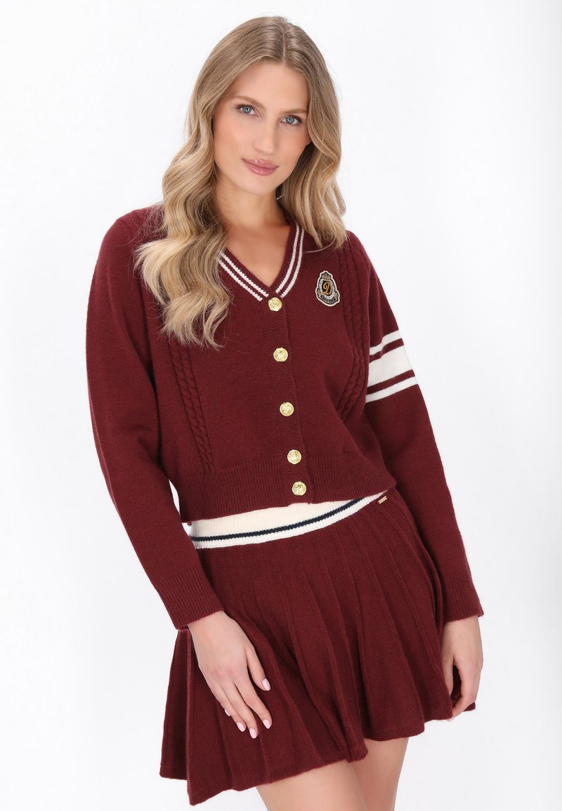 Cardigan lavorato a maglia bordeaux con bottoni dorati, scollatura a V e motivi a treccia, abbinato a una gonna plissettata coordinata con una vita a righe.
