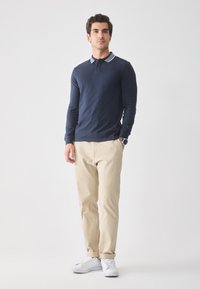 Marineblå langærmet polo med et mønstret krave, parret med beige chinos og hvide sneakers. Outfittet har en afslappet pasform.