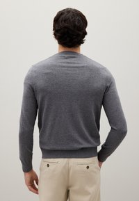 Grauer Strickpullover mit Rundhalsausschnitt, langen Ärmeln und gerippten Bündchen und Saum, kombiniert mit beigen Hosen.