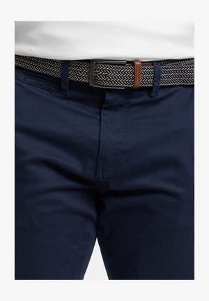 Marinblå byxor med slät framstycke, utrustade med ett texturerat vävt bälte i svart och krämfärgat fiskbensmönster samt bruna läderdetaljer.