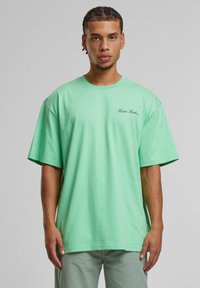 Mint green oversized t-shirt made of cotton with short sleeves and a round neckline. Features "Kani Studios" embroidered on the chest.