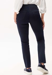 Jeans slim-fit di un blu scuro con vita alta, dotati di due tasche posteriori e dettagli di cucitura sottili, abbinati a sneakers blu navy.