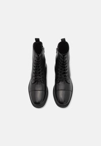 Botas de tobillo de cuero negro con un acabado liso, puntera redonda, cordones en la parte delantera y cremallera lateral. Panel texturizado en el tobillo para añadir detalle.