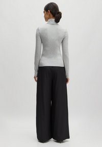 Grijze lange mouw turtleneck top met een getailleerd ontwerp, gecombineerd met wijde zwarte broeken. Zachte textuur, minimalistische stijl.