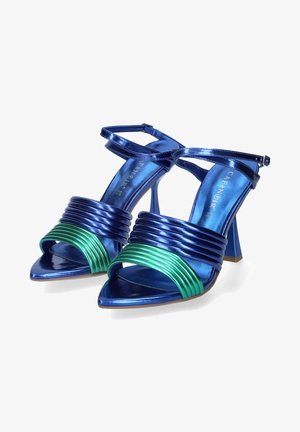 Siniset metallinhohtoiset korkokengät, joissa on vihreät uritetut yksityiskohdat ja ristiin menevät nilkkahihnat. Kengissä on teräväkärkinen muotoilu ja kiiltävä pinta.