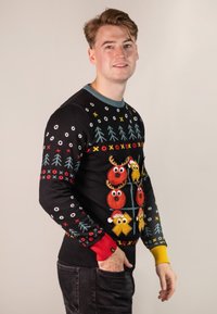 Black sweater with colorful festive patterns, featuring reindeer, ornaments, and trees. Ribbed cuffs in red and yellow, round neckline.