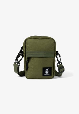 Kompakti oliivivihreä olkalaukku, jossa on säädettävä hihna, etutasku vetoketjulla ja musta bränditunnus, jossa on sarjakuvahahmo.