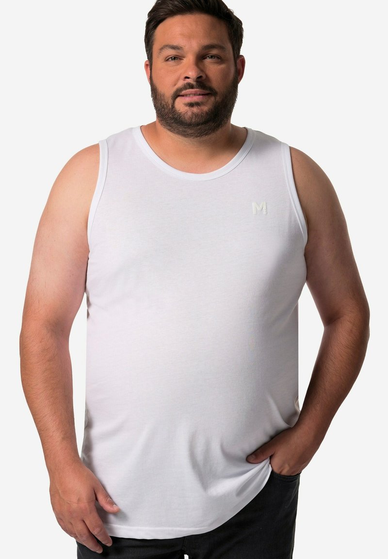 Weißes Baumwoll-Tanktop mit Rundhalsausschnitt, mit dezentem Logo-Stick auf der Brust. Mann steht mit einer Hand in der Tasche und trägt dunkle Jeans.