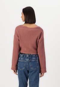 Gekürzter, gerippter Pullover in staubrosa mit weiten Ärmeln, kombiniert mit hochgeschnittenen Denim-Jeans mit elastischem Bund und sog. Fronttaschen.