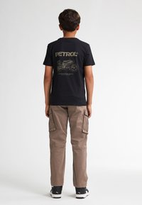 Zwarte katoenen t-shirt met een gouden graphic van een motorfiets en het woord "PETROL" op de achterkant, gecombineerd met beige cargobroeken.