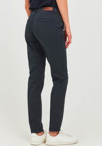 Tmavohnedé, slim-fit nohavice s hladkou textúrou; vybavené koženou nášivkou na páse a na zadných vreckách; skombinované s bielymi teniskami.