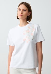 Witte korte mouwen t-shirt gemaakt van gladde katoen, met een bloemenontwerp in roze en goud aan de linkerkant. Eenvoudig ronde hals ontwerp.