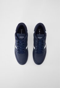 Navyblaue Sneaker mit weißen Streifen, glattem Synthetik-Obermaterial, runder Zehenpartie und Schnürdesign mit dem Lacoste-Logo auf der Zunge.