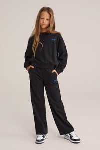 Must must ja sobivad püksid pehmest materjalist, millel on sinine tekst rinnal ja reiel, lõdva istuvuse ja küljetaskutega.