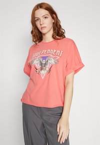 Coral T-shirt featuring a graphic print with an eagle and text "Independent Souls," short sleeves, relaxed fit, soft cotton material.