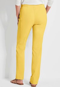 Gele rechte broek van een katoenmix, met achterste plooien voor een goede pasvorm en een platte tailleband, gecombineerd met een licht topje en sandalen.