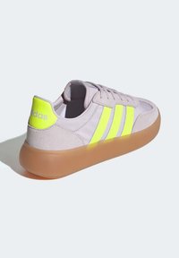 Light purple suede sneaker with three neon yellow stripes, a padded collar, and a rubber sole. Branding visible on the heel.