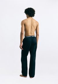 Fekete sportnadrág rugalmas derékkal, rajta "BJÖRG" logóval. Könnyű anyag, egyenes szabás, hátulról látható, meztelen lábakkal.