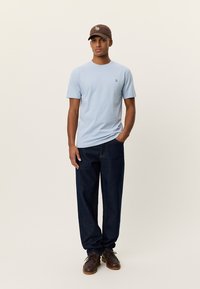 Ανοιχτό μπλε κοντομάνικο T-shirt με μικρό λογότυπο, σε συνδυασμό με σκούρο μπλε τζιν και καφέ παπούτσια. Κα Casual, άνετη εφαρμογή με απλό σχέδιο.