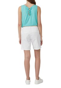 Hellblaues ärmelloses Oberteil mit einer Schleifendetail auf der Rückseite, kombiniert mit weißen hochgekrempelten Shorts und weißen Sneakers.