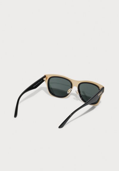 Cat-eye sunglasses with a beige and black frame, dark lenses, and metal accents. Smooth texture with sleek, curved temples.