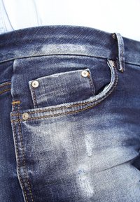 Jeans de mezclilla azul oscuro con una textura desgastada, costuras visibles, un pequeño bolsillo trasero y un desvanecimiento sutil en el material.