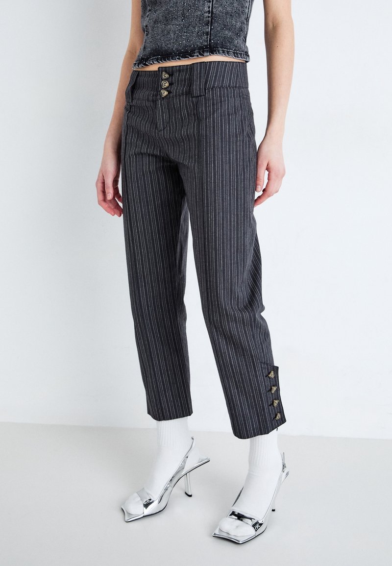 Pantaloni grigi a righe con una vita alta, dotati di tre bottoni decorativi oro. L'orlo ha quattro accenti con bottoni dorati sui lati.