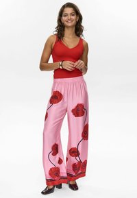 Pantaloni a gamba larga rosa con un motivo floreale di papaveri, cintura elastica e dettagli rossi all'orlo. Abbinati a un top a canotta rosso a coste.