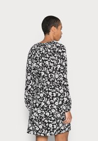 Vestido preto de mangas longas com padrão floral branco, corte descontraído, decote redondo e detalhe franzido nas costas. Comprimento até metade da coxa.