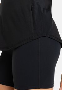 Musta urheilupaita lyhyillä hihoilla, jossa on vetoketjulla varustettu sivutasku. Yhdistetty mustiin tiukkoihin shortseihin, joissa on litteät saumat mukavuutta varten.