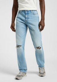 Jeans in denim blu chiaro con una vestibilità rilassata, caratterizzati da strappi visibili sulle ginocchia, design a cinque tasche standard e una leggera scoloritura.
