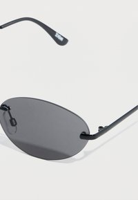 Μαύρα οβάλ γυαλιά ηλίου με σκούρους φακούς, λεπτό μαύρο μεταλλικό πλαίσιο και λεπτά μπράτσα με λεπτομέρεια λογότυπου. Ελαφρύς σχεδιασμός.