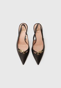 Mustat slingback-kengät teräväkärkisillä, sileästä nahasta valmistetuilla, kullanvärisillä varusteilla ja leikatuilla yksityiskohdilla. Pehmeät beige sisäpohjat näkyvissä.