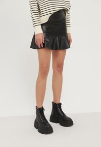Donna che indossa una minigonna in pelle nera con bordo arricciato, stivali platform neri con lacci, e un maglione a righe crema e nere.