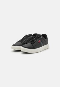 Schwarze Leder-Sneaker mit niedrigem Profil, weißer Gummisohle, Schnürdesign und kleinem roten Logo an der Seite. Glatte Textur und minimalistische Akzente.