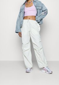 Joggers bianchi leggeri con polsini elastici, abbinati a un top corto lavanda con la scritta "LEVI'S CALIFORNIA" e una giacca di jeans. Sneakers argento.