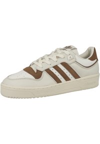Białe skórzane sneakersy z brązowymi zamszowymi akcentami, trzema brązowymi paskami, perforowanym noskiem oraz teksturowaną gumową podeszwą. Logo na języku i pięcie.