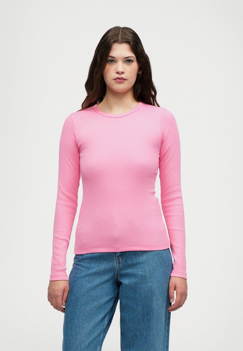 Ružičasta majica dugih rukava s okruglim izrezom, uskog kroja i glatke teksture, u kombinaciji s svijetloplavim trapericama.