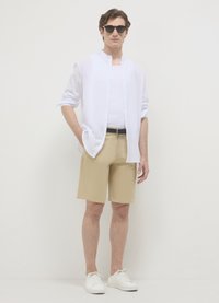 White button-up shirt over a white tank top, beige shorts, and white sneakers. Sunglasses complete the casual outfit. Minimalistic design.