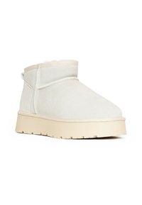 Stivaletti corti in suede avorio con una morbida fodera, punta arrotondata e suola beige spessa e testurizzata. Presentano una cucitura minimale e un anello sul retro.