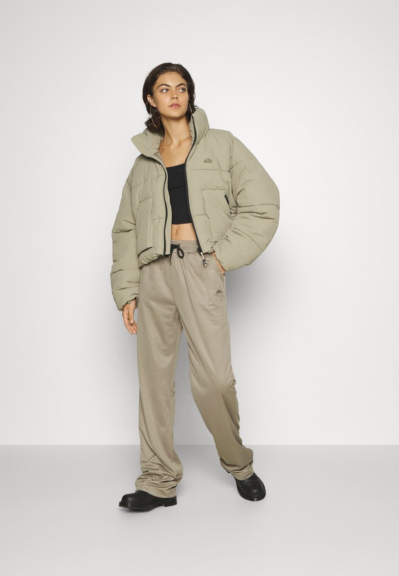 Krótkia puchowa kurtka w jasnym oliwkowym kolorze, z przesadnie dużymi rękawami, wysokim kołnierzem i kieszenią z przodu. Zestawiona z beżowymi spodniami o luźnym kroju.