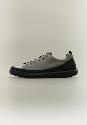 Baskets basses avec dessus gris, semelle noire et talon noir, lacets gris et col rembourré sur fond uni.
